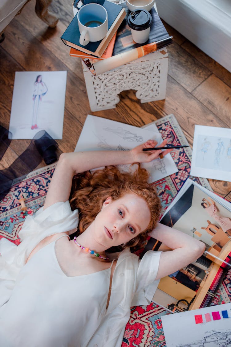 Woman Lying Down On Floor Carpet With Sketch Drawing On Paper