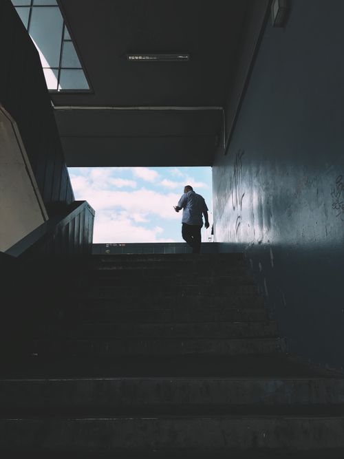 Free Back view of distant anonymous male walking upstairs with railings while getting out of underground crossing in city against blue sky Stock Photo