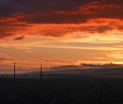 A striking sunrise over a rural countryside with dramatic clouds and open fields.