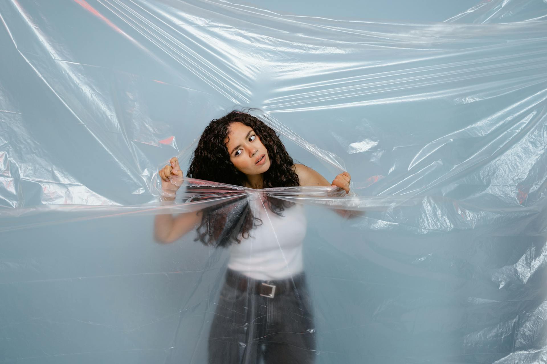 A woman tearing through a plastic sheet on a blue background, symbolizing freedom.