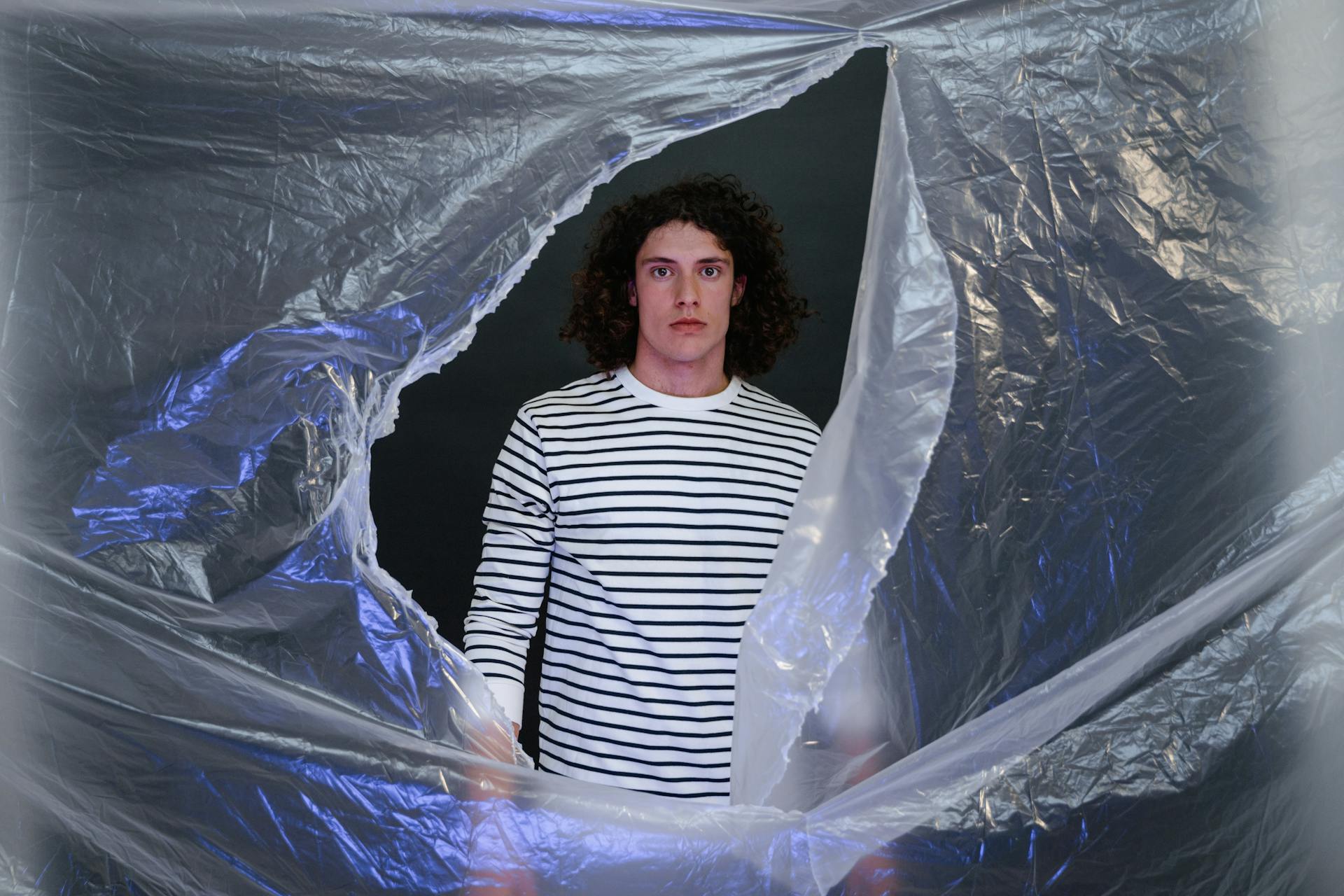 A man standing amid torn plastic foil symbolizes confronting pollution and environmental challenges.