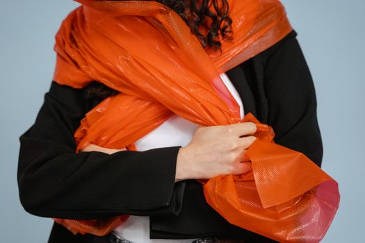 Artistic photo of a person wrapped in vibrant orange recycled materials, highlighting fashion and sustainability.