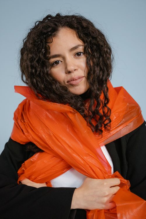 Free A thoughtful woman with curly hair wrapped in a striking orange scarf, emphasizing fashion and style. Stock Photo