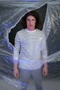 Young Man in Striped Long Sleeve Shirt Standing in Front of a Ripped Plastic