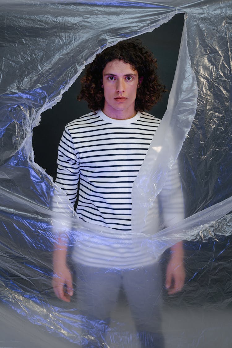 Young Man In Striped Long Sleeve Shirt Standing In Front Of A Ripped Plastic