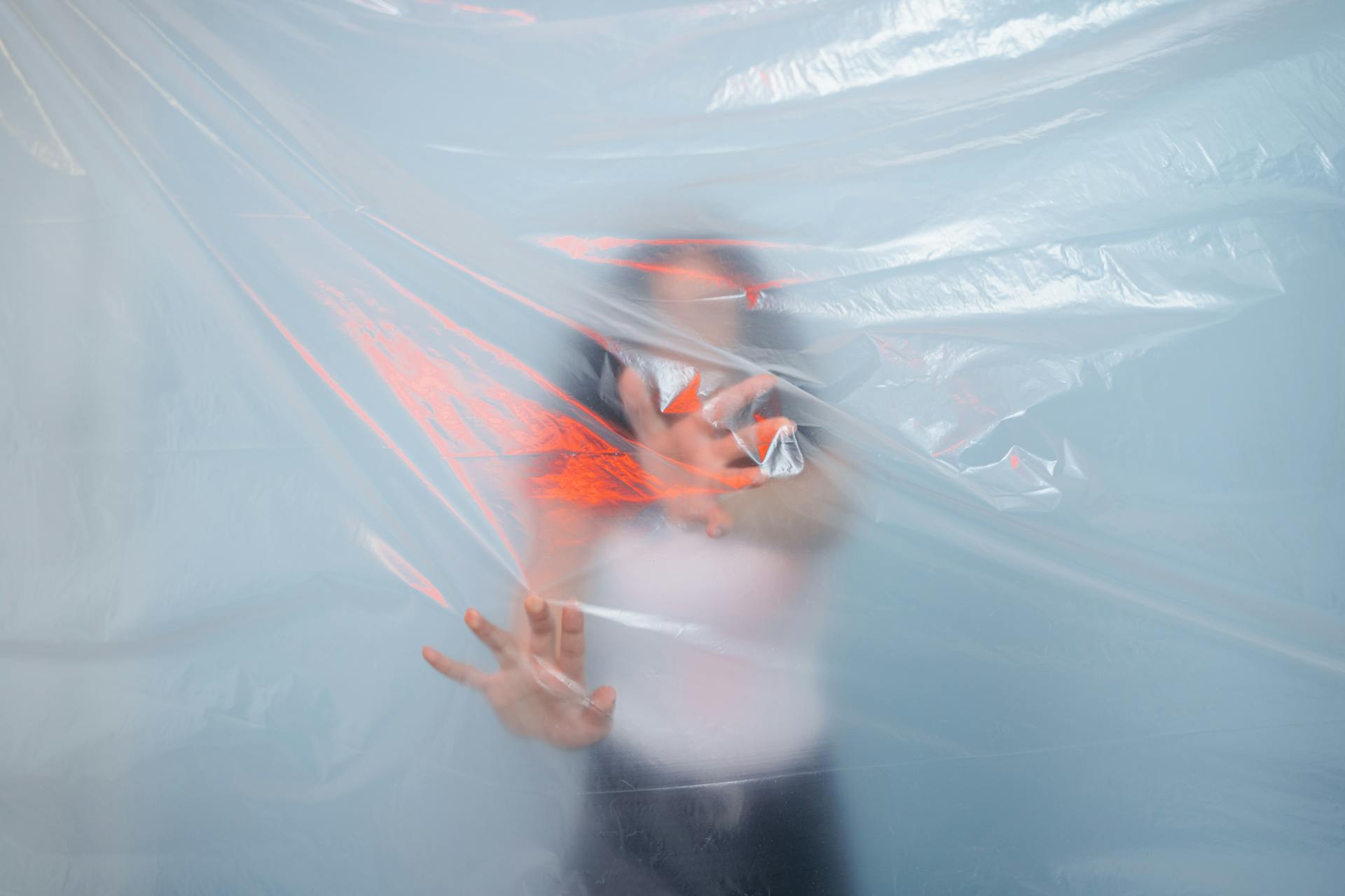 A person stands behind a translucent plastic sheet, symbolizing pollution and environmental issues.