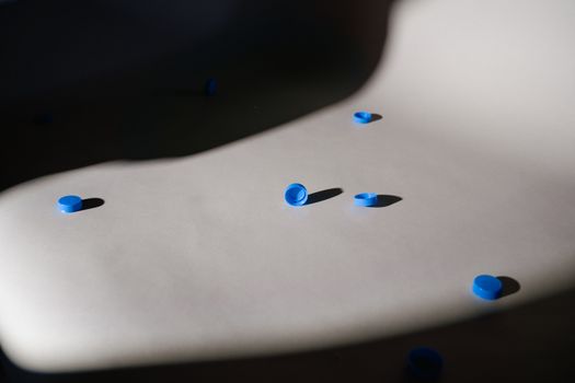 Artistic arrangement of blue bottle caps casting shadows on a smooth surface.