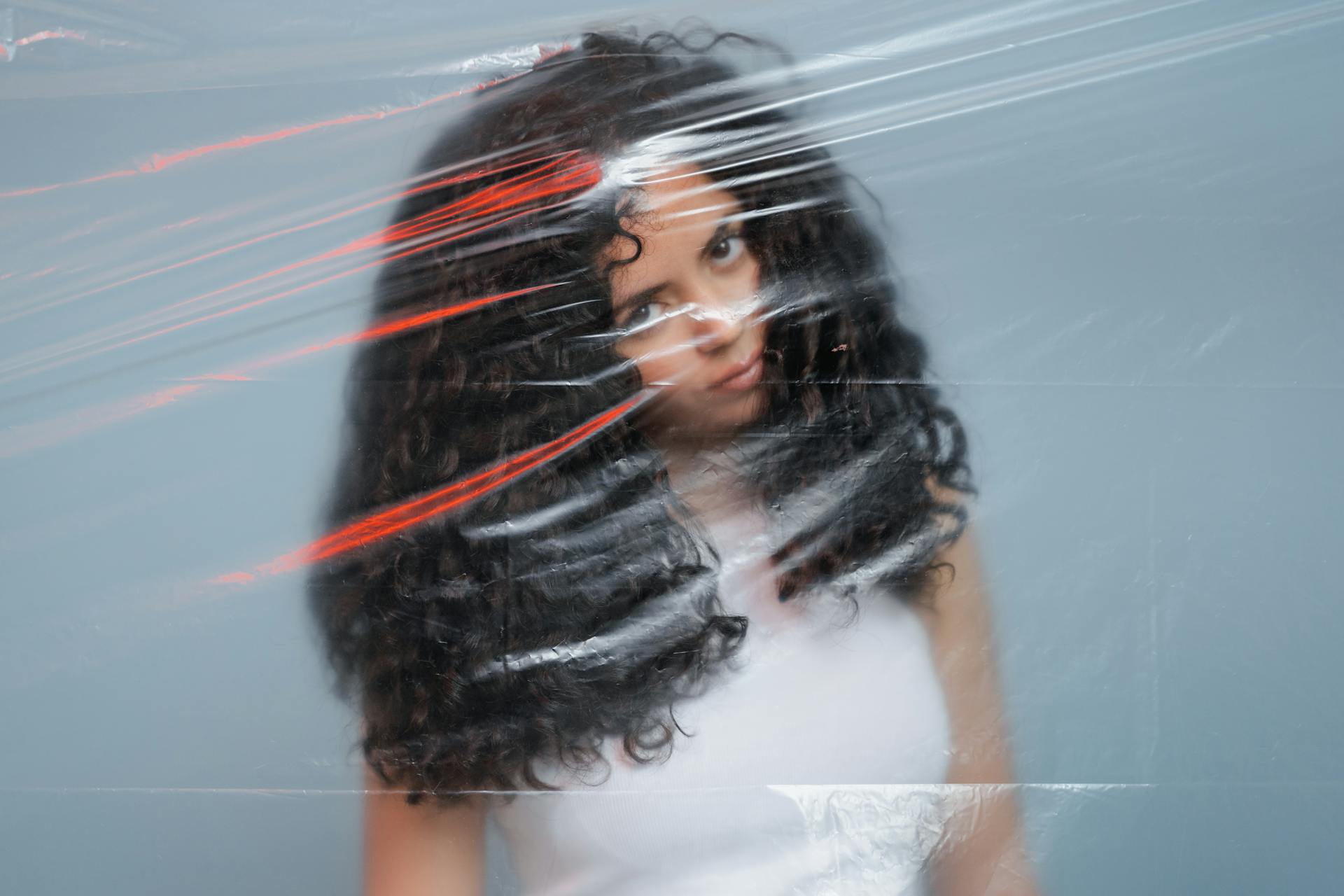 Creative portrait of a woman with curly hair through plastic film, evoking a unique visual effect.