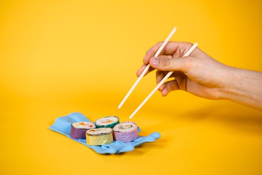 Artistic sushi on a rubber glove with chopsticks, set against a vibrant yellow background.