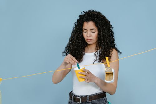 Free Young woman engaged in creative painting in a studio. Minimalist setup with light blue background. Stock Photo