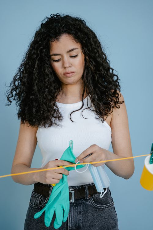 Free Young woman holding gloves against a light blue backdrop, preparing for cleaning. Stock Photo