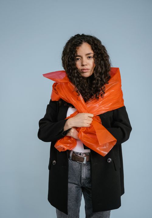 Free Fashionable woman wearing an orange plastic scarf over a coat against a blue background. Stock Photo