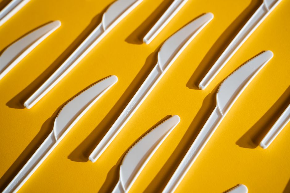 Minimalist arrangement of white plastic knives on a bright yellow background.