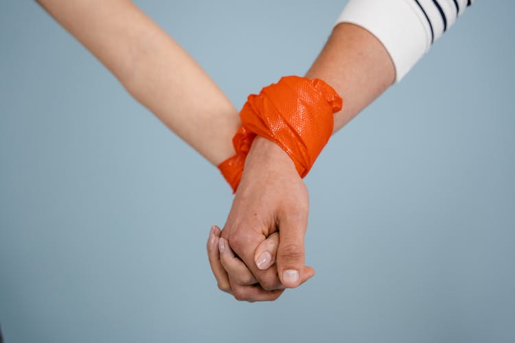 People Holding Hands With A Plastic Tied On Their Wrists