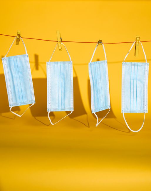 Four blue face masks hanging on a line against a bright yellow background.