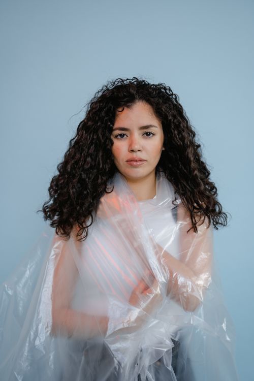 Free Artistic portrait of a woman enveloped in a clear plastic sheet, set against a soft blue background. Stock Photo