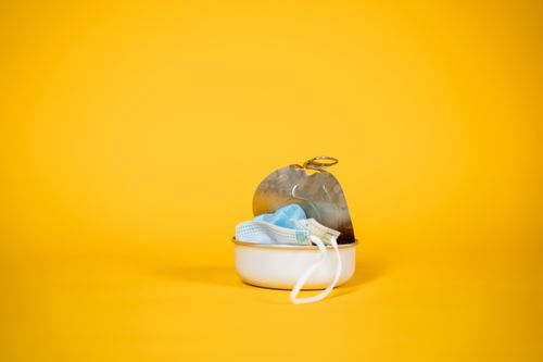 Free Close-up of a face mask in an open tin can against a bright yellow background, symbolizing pollution and waste. Stock Photo