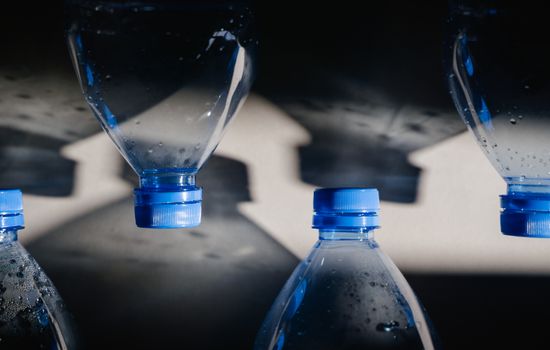 Close-up of plastic bottles with blue caps casting shadows, highlighting recycling themes.