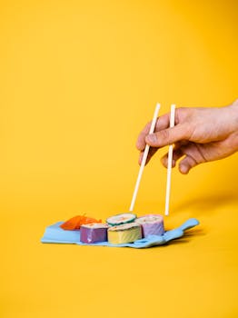 Colorful sushi rolls with chopsticks on a bright yellow backdrop, highlighting Asian cuisine.
