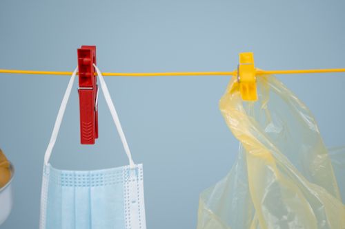 Free A face mask and plastic bag hang on a clothesline against a blue background. Stock Photo