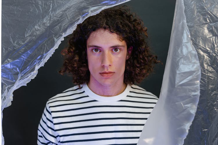 A Man Wearing A Striped Shirt Standing Behind A Torn Plastic Sheet