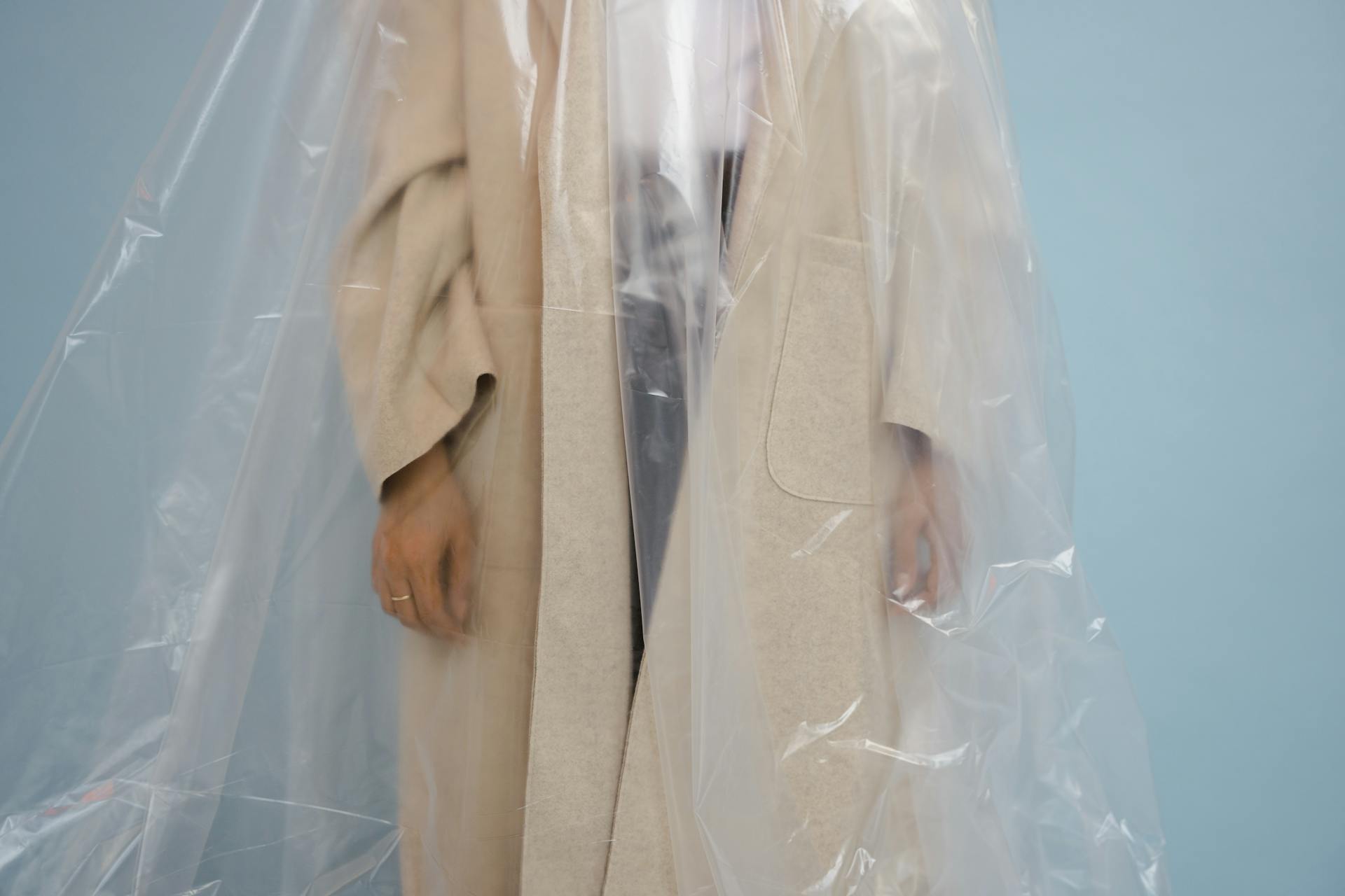 Faceless portrait of a person in a beige coat covered with clear plastic film.