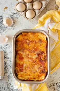 Delicious homemade lasagna in baking dish surrounded by eggs and kitchen utensils.
