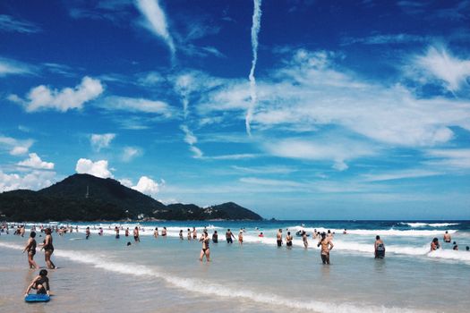 Crowded beach with people enjoying the water and scenic mountains in Ubatuba, Brazil.
