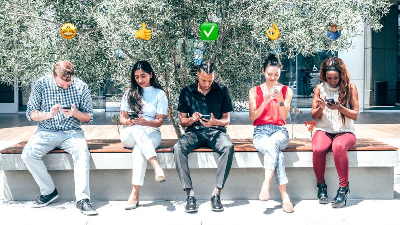 A diverse group of people sitting outdoors together, each looking at their phones