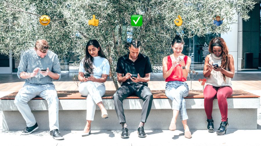 A diverse group of people sitting outdoors together, each looking at their phones