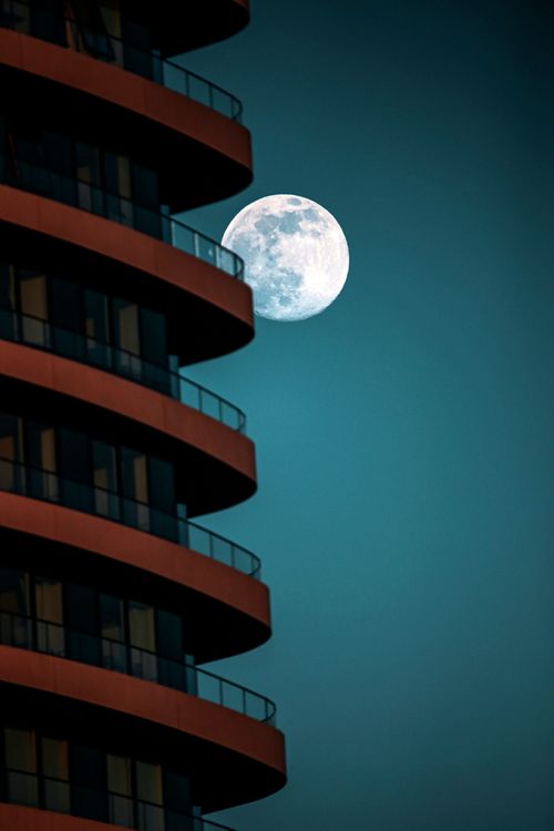 Free A striking view of a modern building silhouette juxtaposed with a full moon in England. Stock Photo