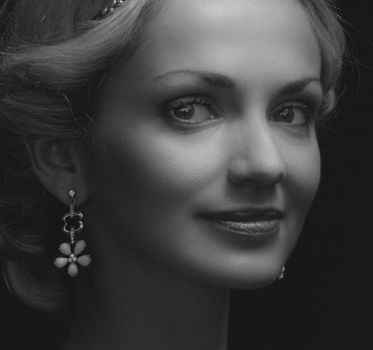 A refined grayscale portrait of a smiling woman wearing earrings.
