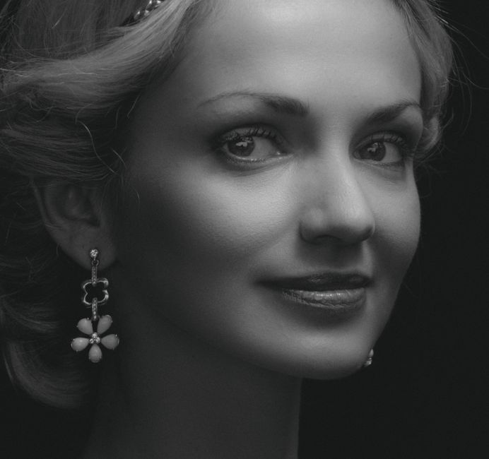 A refined grayscale portrait of a smiling woman wearing earrings.