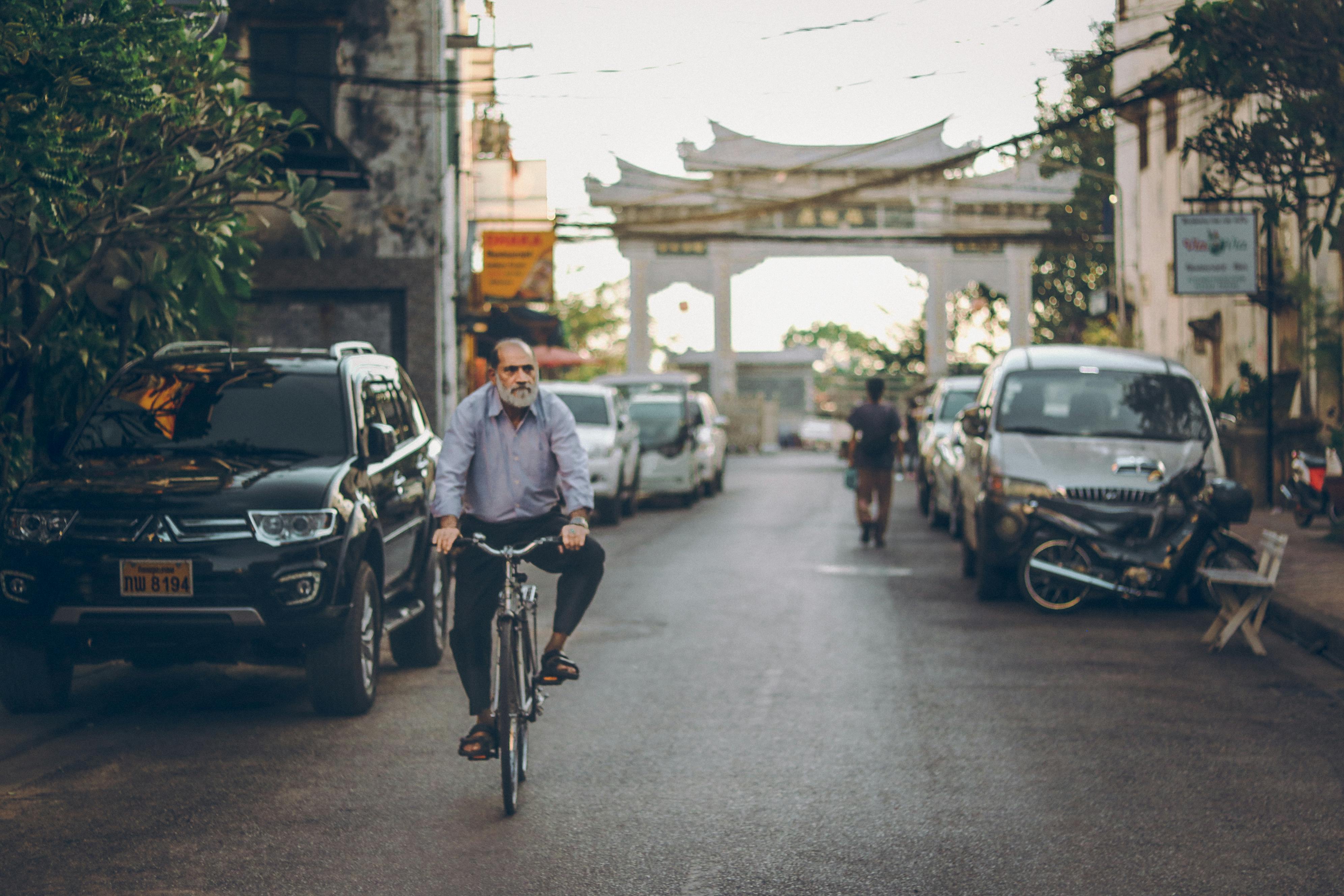 一名男子在安静的街道上骑自行车，背景是停放的汽车和文化建筑