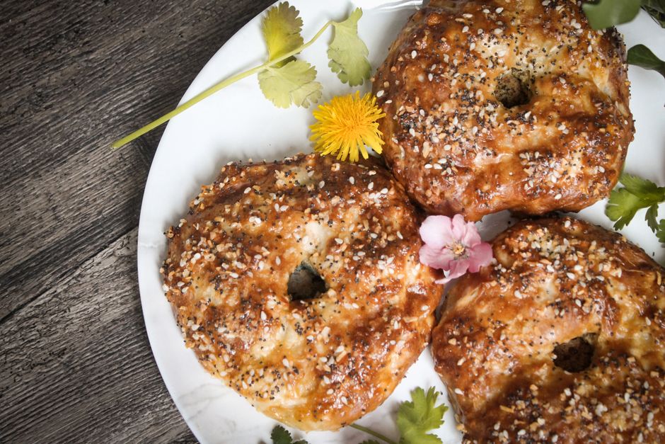 A row of golden-brown sourdough bagels topped with everything seasoning and sesame seeds, cooling on a wire rack.