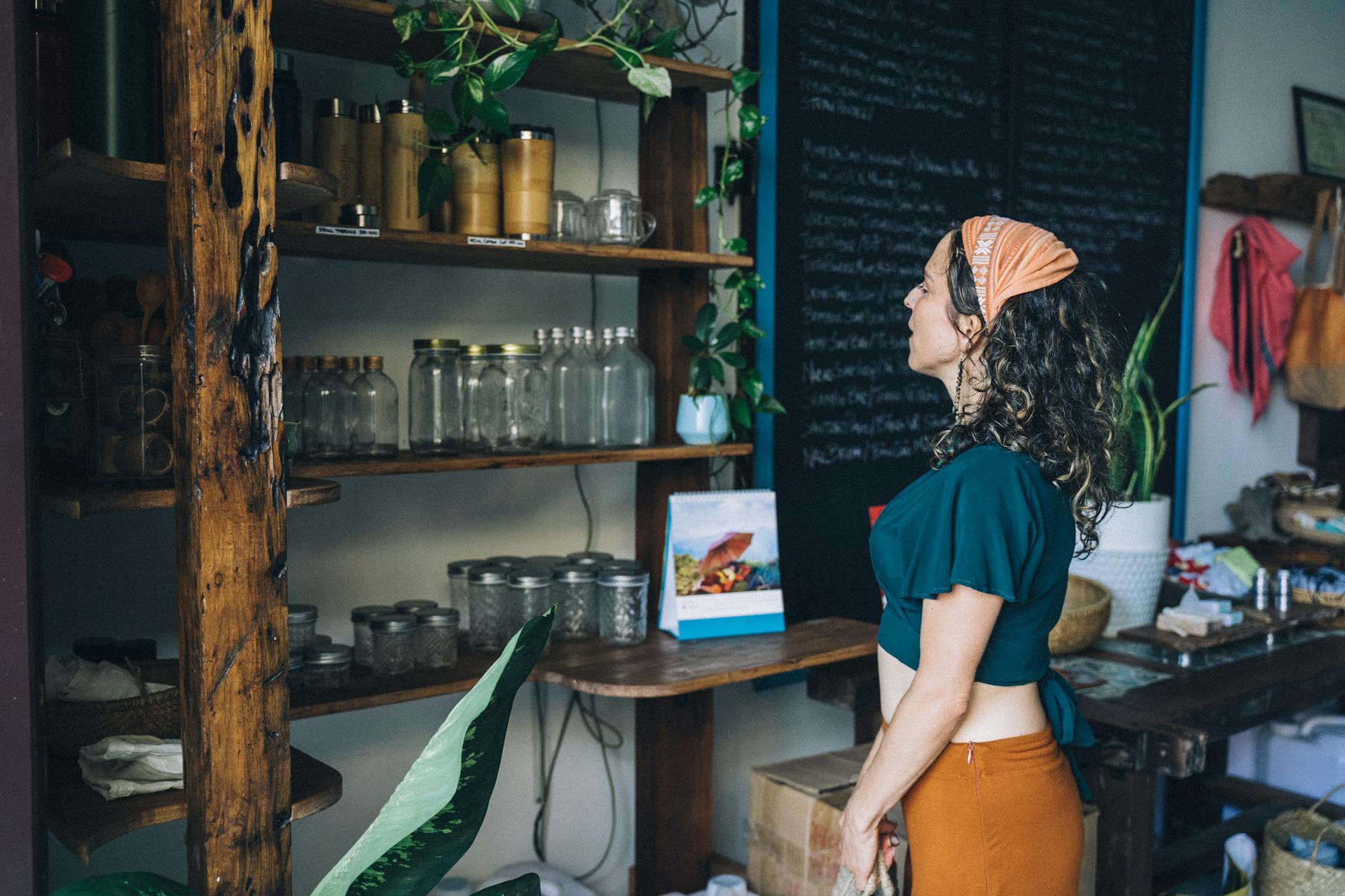 Curly-haired woman in eco-friendly shop browsing jars on rustic wooden shelves.