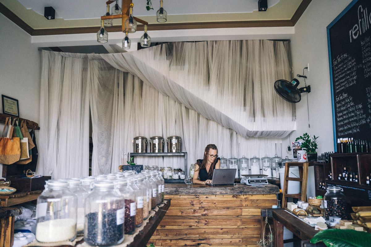 Shopkeeper using a laptop at the counter of a small refill store with glass jars on the shelves