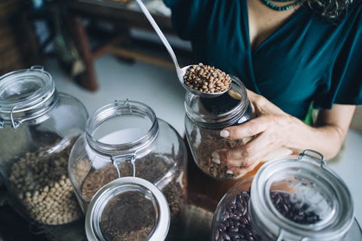 Person refilling reusable glass jars with various beans in an eco-friendly store.