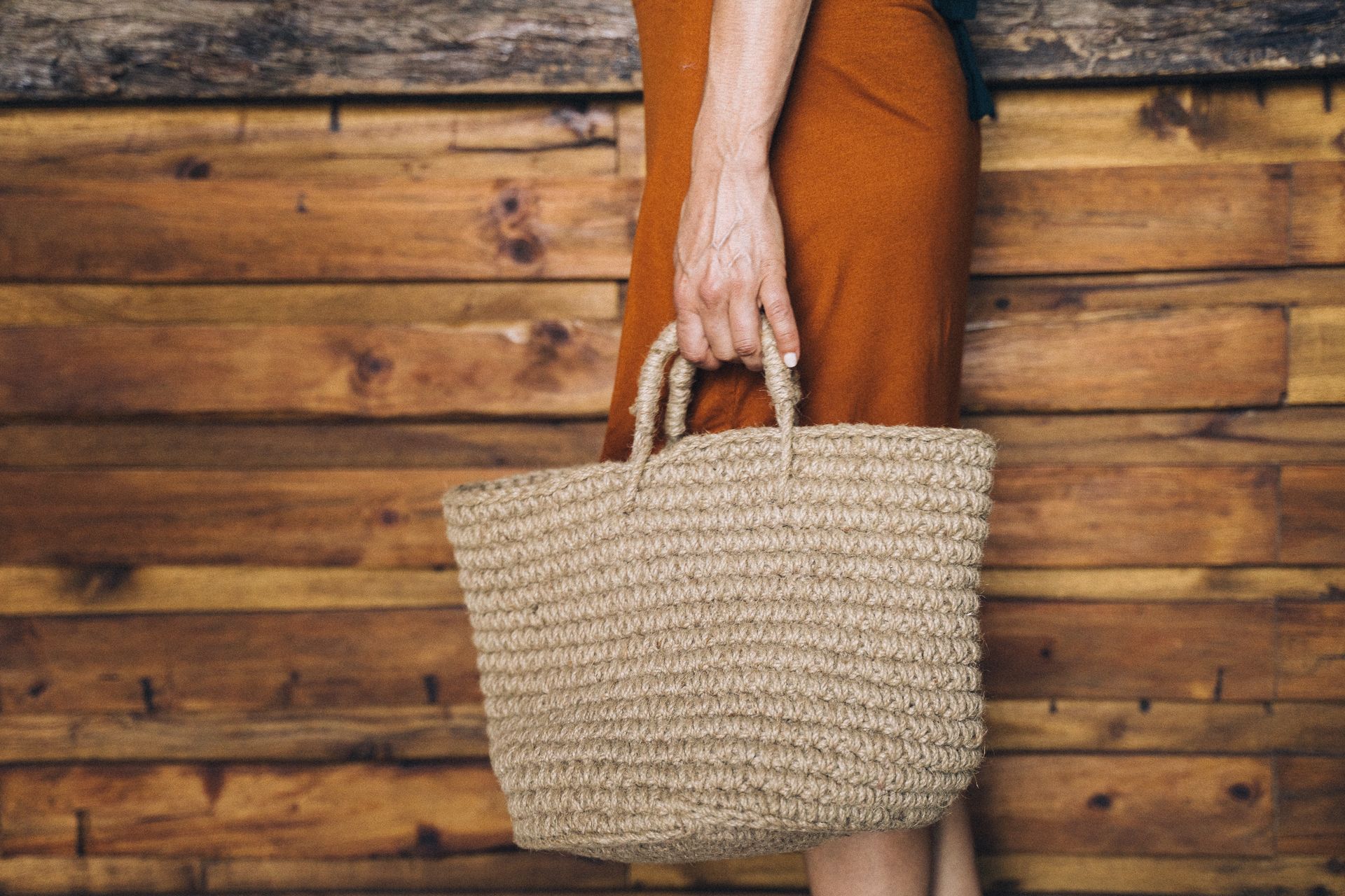 A close-up of a hand holding a sustainable woven bag against a wooden background.