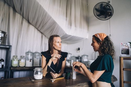 Free Two women engaging in conversation at an eco-friendly store with glass jars and refillable products. Stock Photo