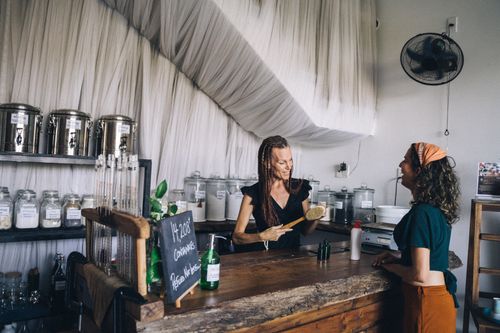 Free Two women engaging at an eco-friendly shop counter with refillable containers and glass jars. Stock Photo