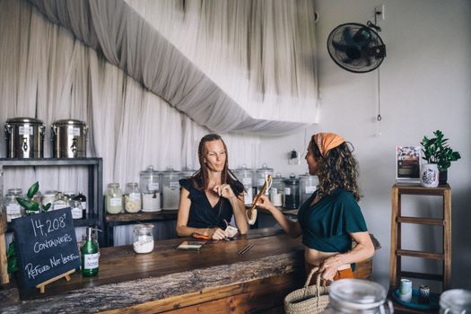 Two women shopping in an eco-friendly store with refillable glass jars and organic products.