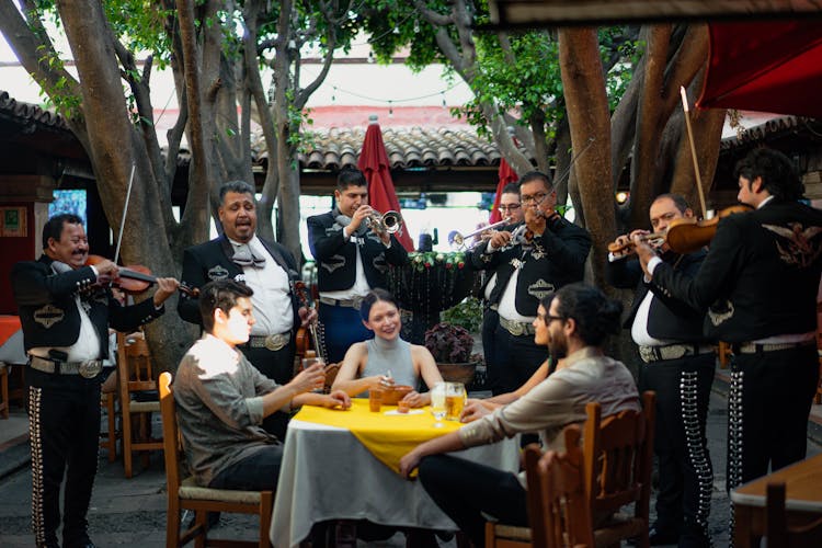 Group Of Friends Eating While Listening To Mariachi Band