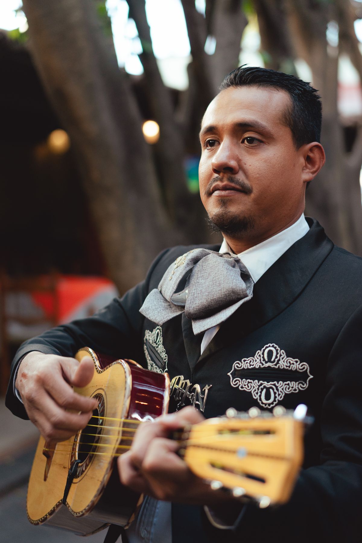 A mariachi musician in traditional attire playing a guitar outdoors on a sunny day.