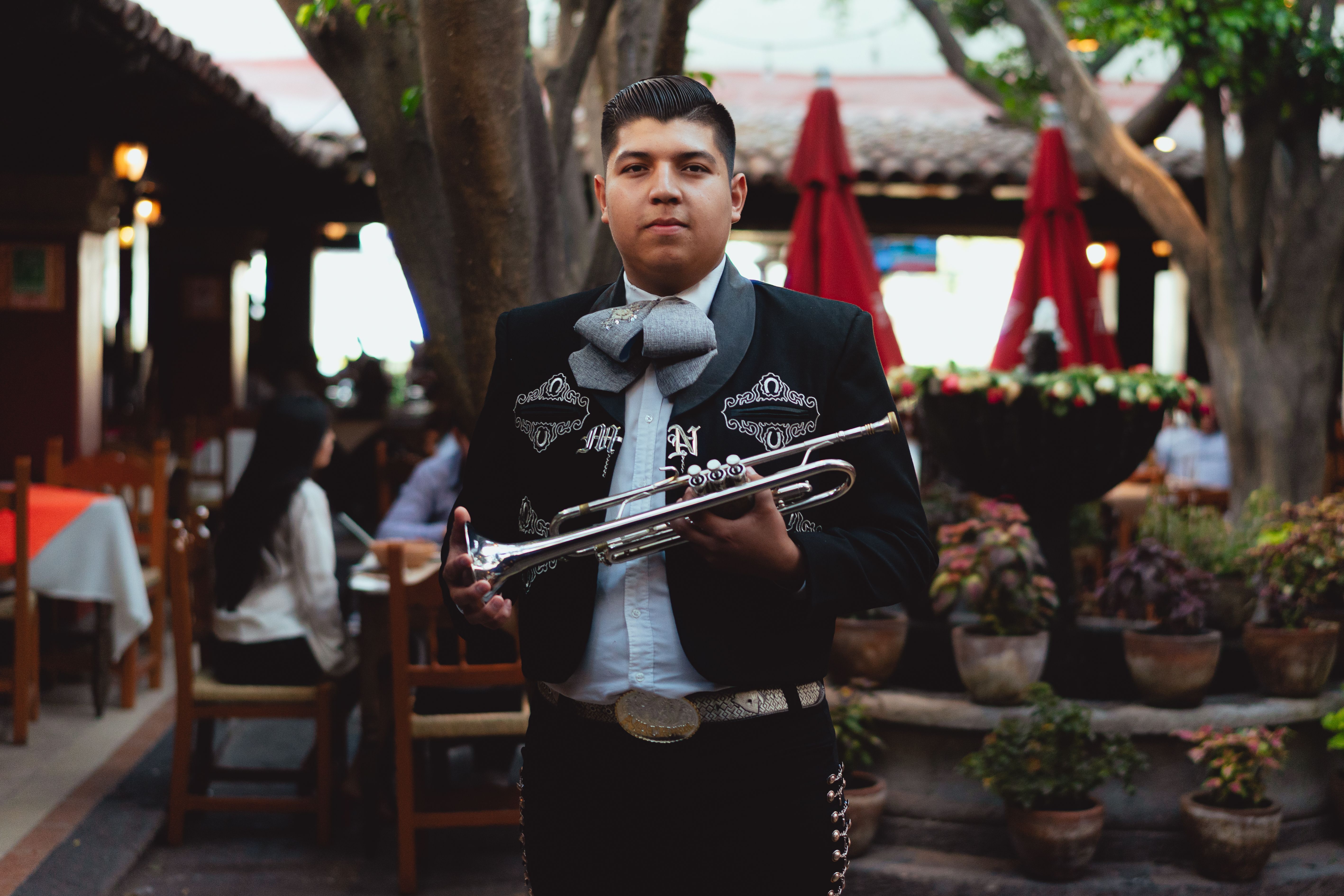 A mariachi musician in traditional attire holding a trumpet indoors at a Mexican restaurant.