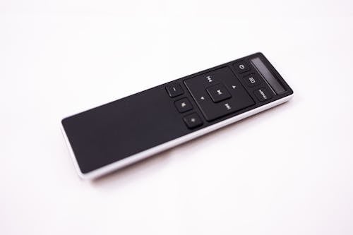 Isolated dark contemporary remote control with buttons placed on white surface in studio