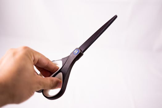 Isolated unrecognizable crop person showing black sharp scissors in hand against blank wall