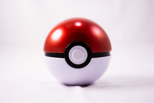 A closeup of a red and white toy ball on a smooth white surface, reflecting light.