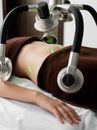 Crop anonymous female client lying under green lasers on belly while receiving fat loss treatment in modern light medical clinic