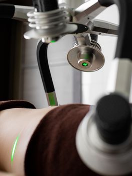Crop unrecognizable patient lying under green lasers of contemporary weight loss machine with heads during slimming treatment in light modern medical clinic